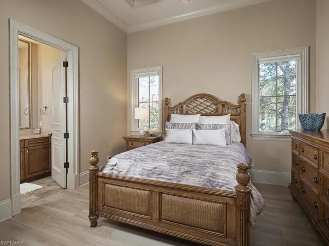 Bedroom with light wood finished floors, crown molding, and connected bathroom