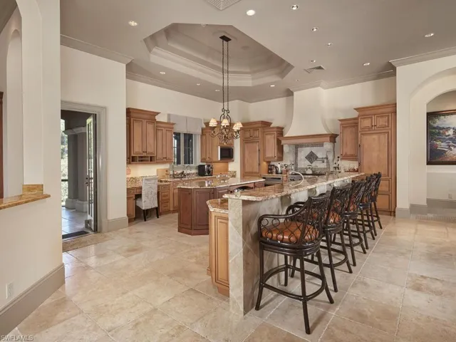 Kitchen with wood finish cabinetry, ornamental molding, a kitchen breakfast bar, arched walkways, and light stone countertops