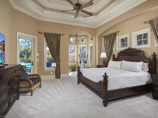 Carpeted bedroom featuring access to exterior, a ceiling fan, a tray ceiling, multiple windows, and a chandelier