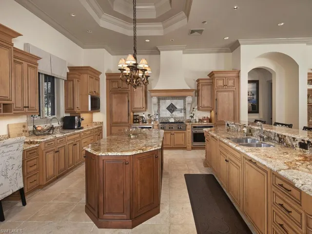 Kitchen featuring ornamental molding, light stone countertops, wood finish cabinetry, stainless steel appliances, and a kitchen island