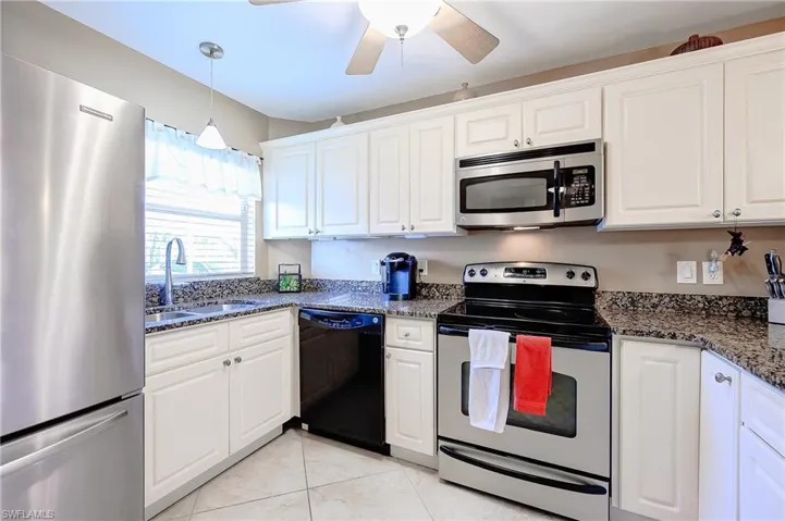 Kitchen with appliances with stainless steel finishes, white cabinetry, dark stone counters, hanging light fixtures, and light tile patterned flooring