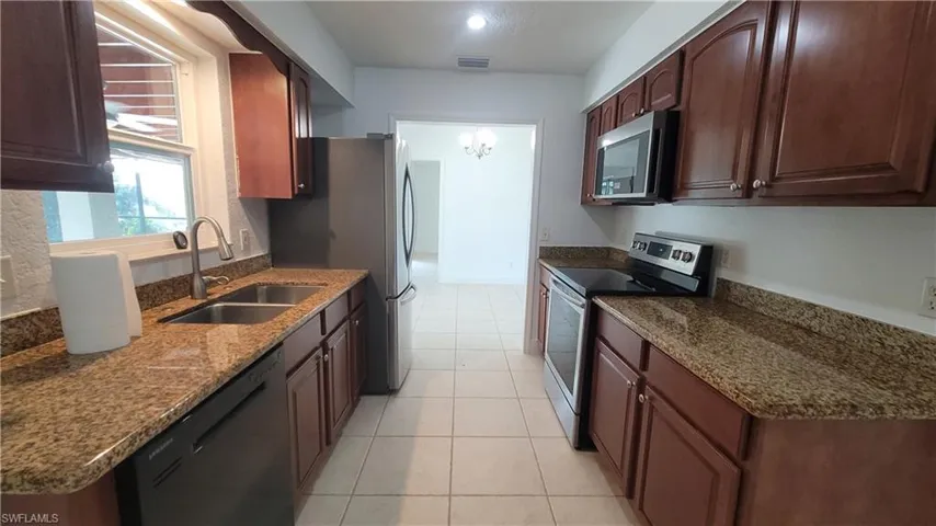 Kitchen featuring stone counters, appliances with stainless steel finishes, light tile patterned flooring, and sink