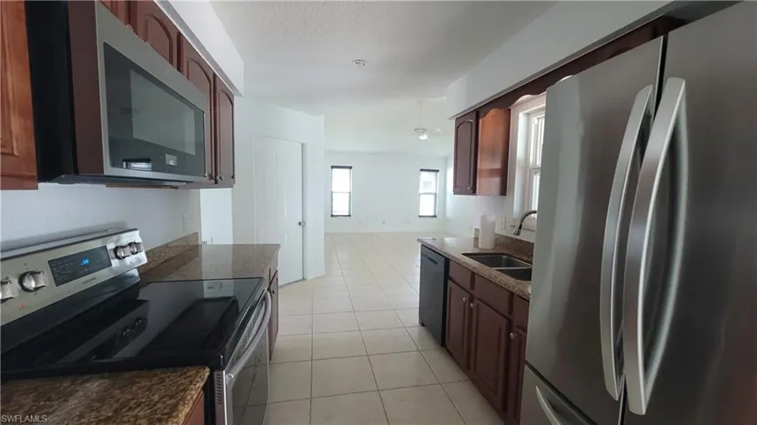 Kitchen featuring a textured ceiling, sink, light tile patterned floors, and stainless steel appliances