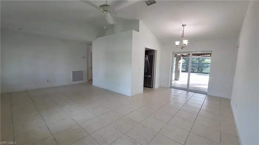 Tiled spare room with ceiling fan with notable chandelier and lofted ceiling