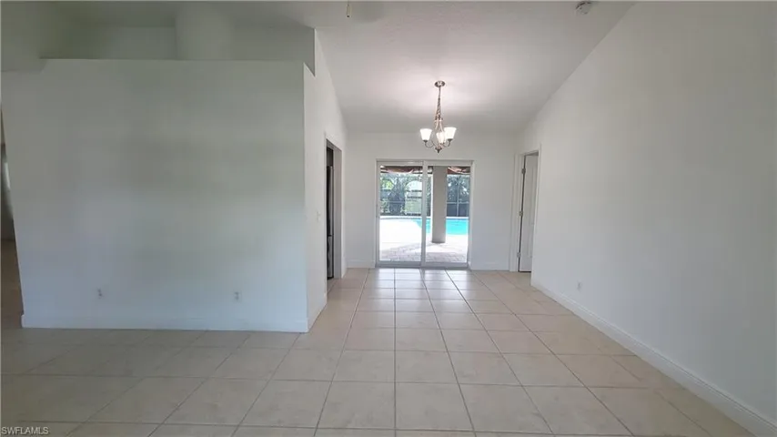Empty room with light tile patterned floors and a notable chandelier