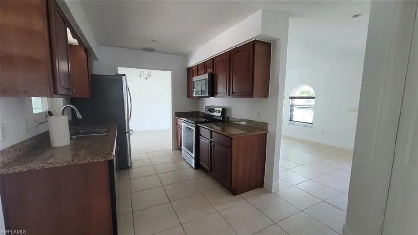 Kitchen with sink, dark stone countertops, dark brown cabinets, light tile patterned floors, and appliances with stainless steel finishes