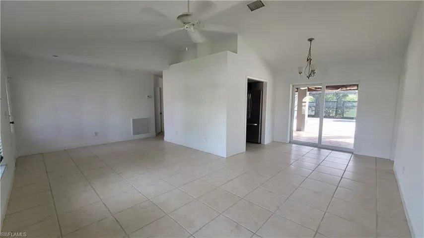 Tiled spare room with ceiling fan with notable chandelier and vaulted ceiling