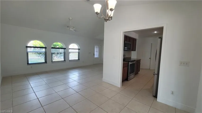 Empty room with ceiling fan with notable chandelier, light tile patterned floors, and vaulted ceiling