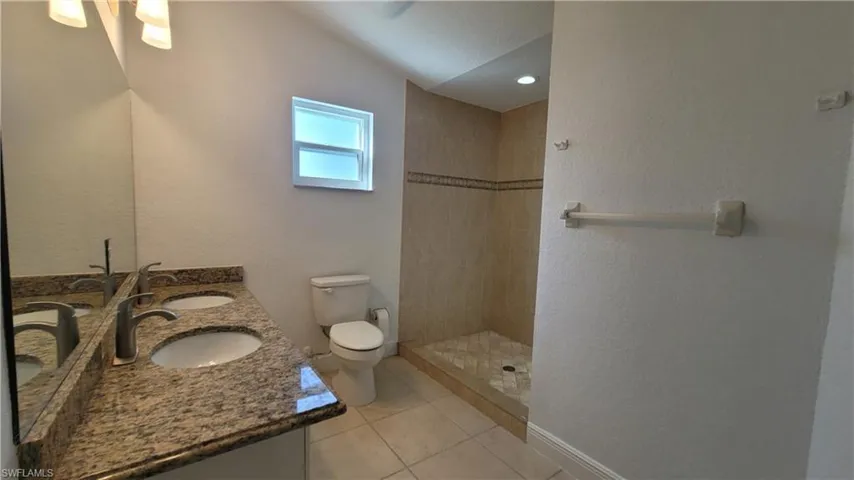 Bathroom featuring a tile shower, tile patterned flooring, vaulted ceiling, toilet, and vanity