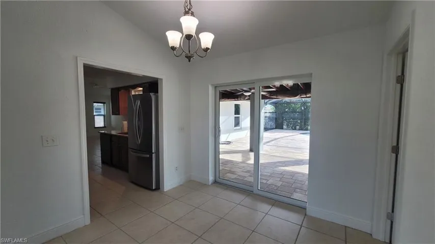 Unfurnished dining area featuring light tile patterned floors, lofted ceiling, and a notable chandelier