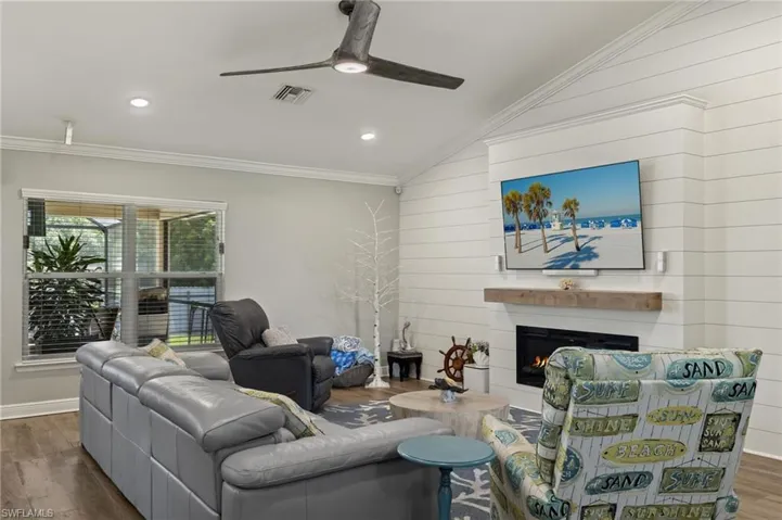 Living room featuring wood walls, wood-type flooring, crown molding, lofted ceiling, and ceiling fan