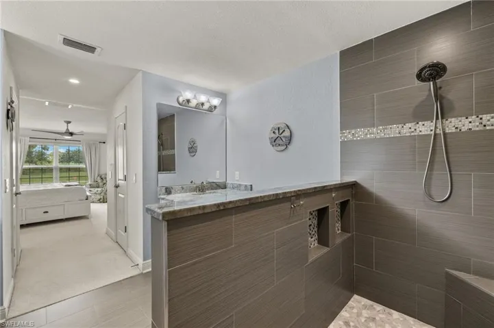 Bathroom with tiled shower, ceiling fan, a textured ceiling, and vanity