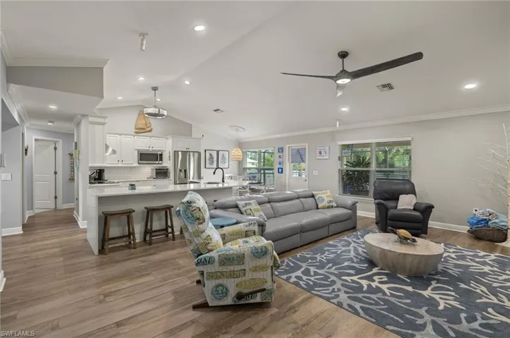 Living room with lofted ceiling, ceiling fan, ornamental molding, and light wood-type flooring