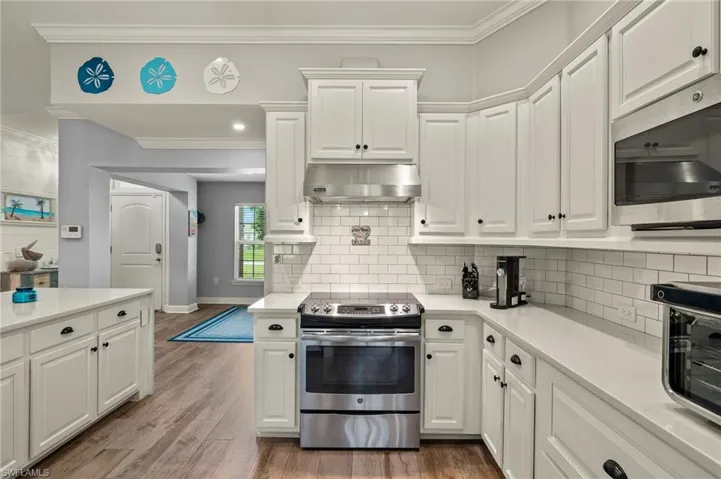Kitchen featuring wood-type flooring, ornamental molding, appliances with stainless steel finishes, and white cabinets