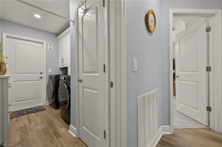 Laundry room with washing machine and clothes dryer, cabinets, and light hardwood / wood-style floors