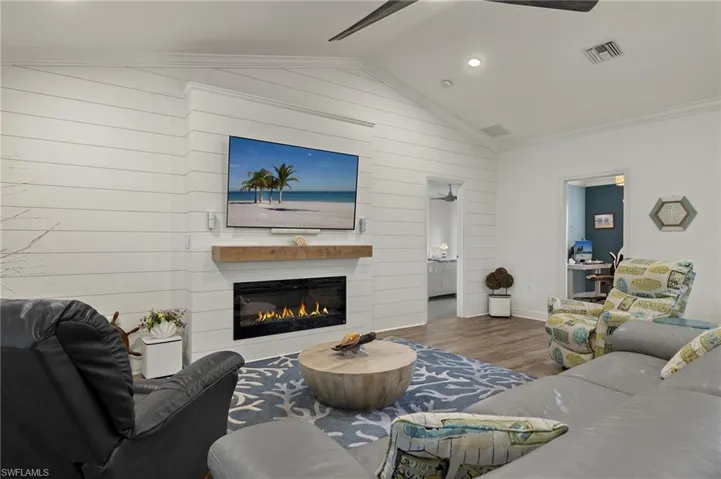 Living room featuring vaulted ceiling, hardwood / wood-style floors, wood walls, ceiling fan, and ornamental molding