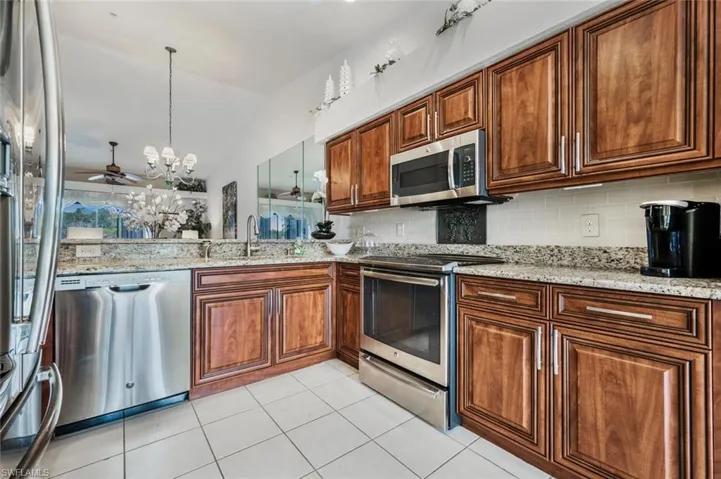 Kitchen with appliances with stainless steel finishes, a chandelier, light stone counters, pendant lighting, and lofted ceiling