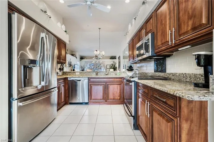 Kitchen featuring appliances with stainless steel finishes, light stone counters, a chandelier, decorative light fixtures, and decorative backsplash