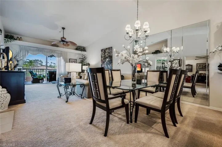 Dining space with a ceiling fan, light colored carpet, high vaulted ceiling, and a chandelier