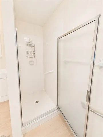 Spacious shower enclosure featuring white subway tile surround, clear glass shower door with metal framing, and a contrasting light wood-finish flooring outside