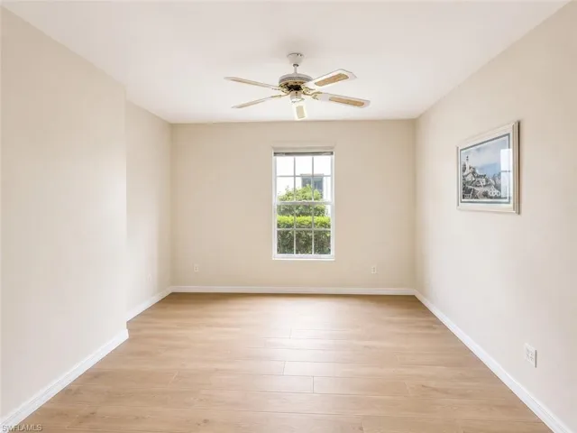 Spacious room featuring light-toned walls, wood-finish flooring, a ceiling fan, and a double-hung window