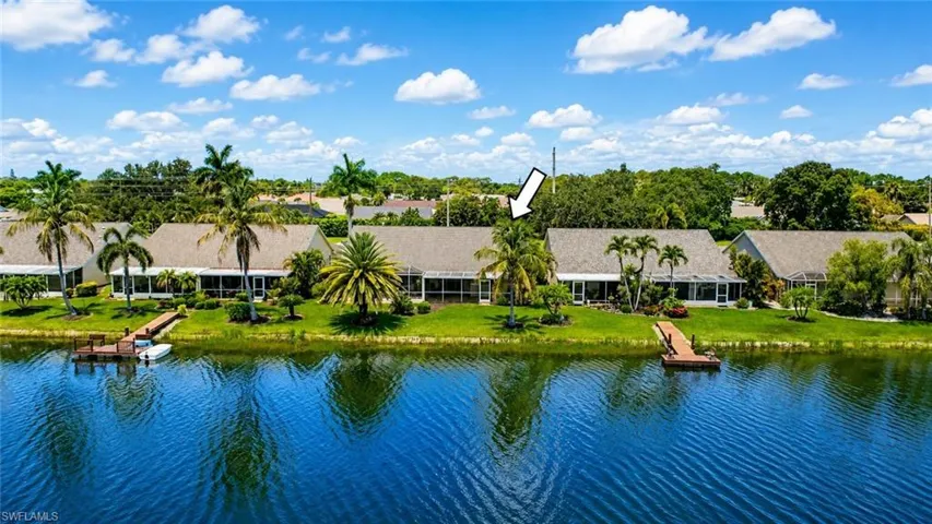 Waterfront property featuring a private dock, expansive green space, and mature palm trees