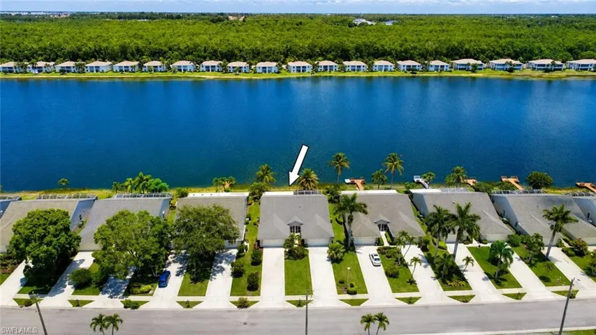 Waterfront property featuring a private dock, mature palm trees, manicured landscaping, and a driveway with an attached garage