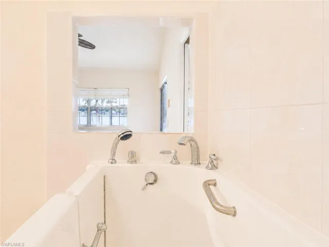 White tiled shower surround featuring a built-in tub with chrome fixtures, a handheld showerhead, and an integrated grab bar