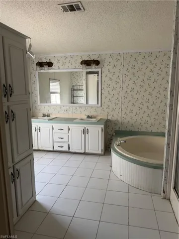 Bathroom featuring visible vents, wallpapered walls, tile patterned floors, a textured ceiling, and a sink