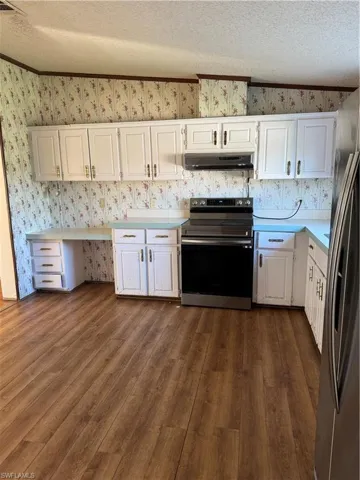 Kitchen with wallpapered walls, refrigerator, light countertops, exhaust hood, and range