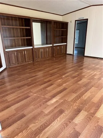 Spare room featuring ornamental molding, built in shelves, a textured ceiling, and wood finished floors