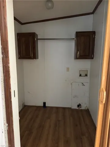 Clothes washing area featuring dark wood-style floors, cabinet space, hookup for a washing machine, and crown molding