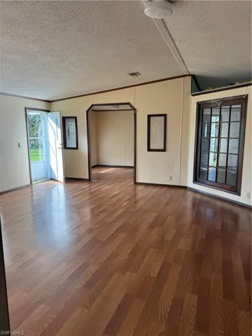 Empty room featuring wood finished floors, visible vents, arched walkways, a textured ceiling, and crown molding