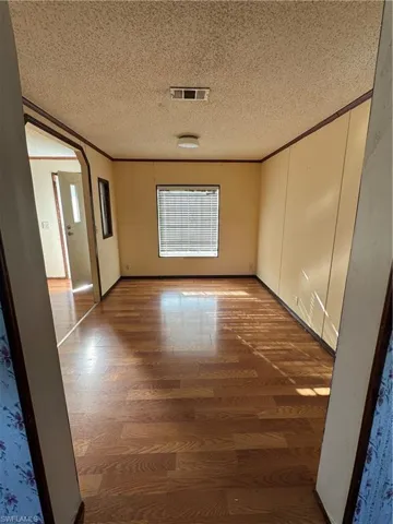 Unfurnished room featuring arched walkways, visible vents, crown molding, and wood finished floors
