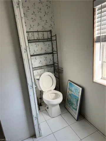 Bathroom with wallpapered walls, toilet, and tile patterned flooring