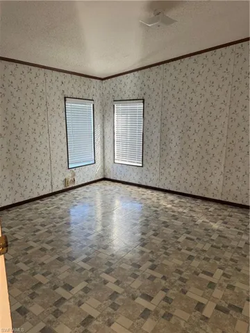 Unfurnished room with a textured ceiling, crown molding, and wallpapered walls