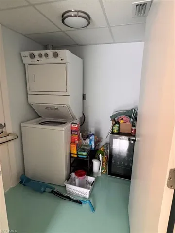 Laundry room featuring a paneled ceiling, stacked washing machine and dryer, and concrete flooring