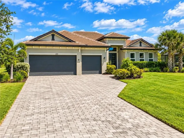 Single-story home featuring a paver driveway, two-car garage, manicured lawn, and tropical landscaping