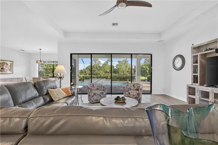 Tray ceiling with ceiling fan, expansive sliding glass doors, engineered wood flooring, built-in entertainment center, and recessed lighting
