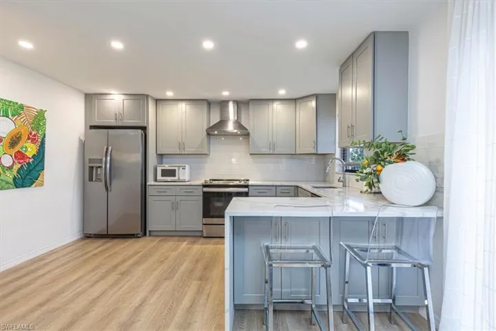 Kitchen featuring gray cabinetry, stainless steel appliances, light stone counters, a kitchen breakfast bar, and light wood finished floors