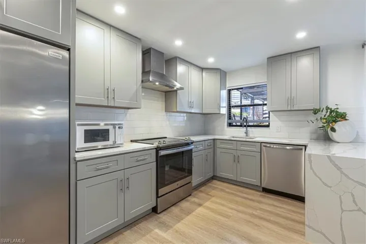 Kitchen with gray cabinetry, stainless steel appliances, light stone counters, recessed lighting, and light wood finished floors