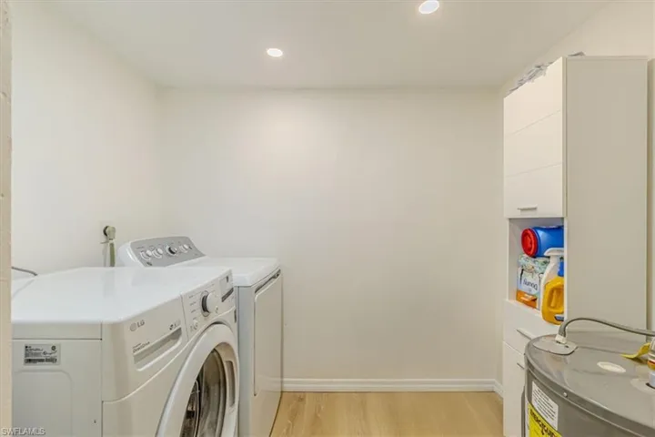 Laundry area with electric water heater, light wood-style flooring, washing machine and dryer, and recessed lighting