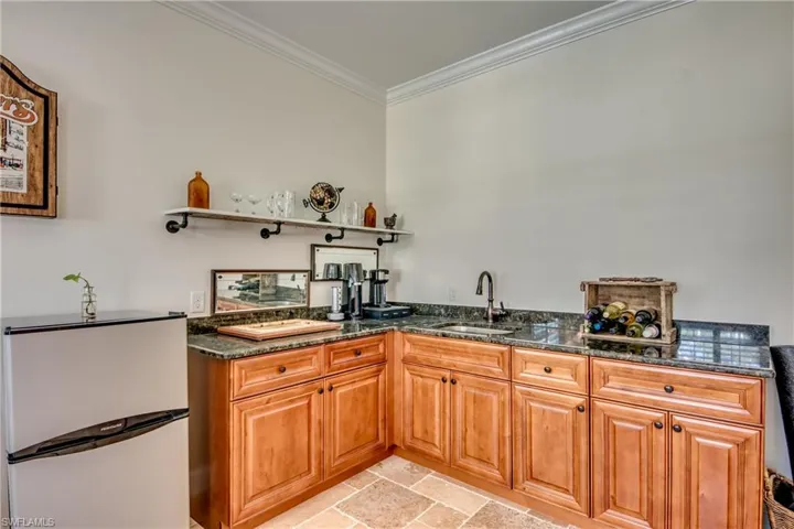 Kitchen with dark stone countertops, crown molding, light tile patterned floors, stainless steel fridge, and sink
