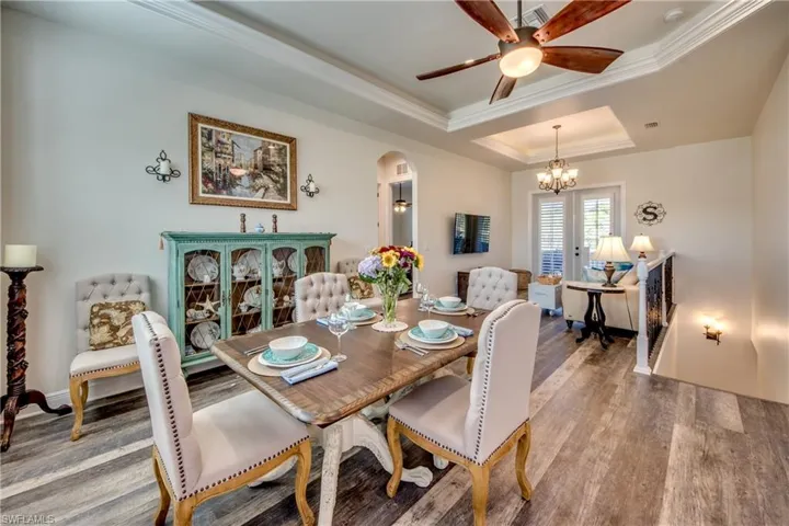 Dining space featuring ceiling fan with notable chandelier, a raised ceiling, crown molding, and hardwood / wood-style floors
