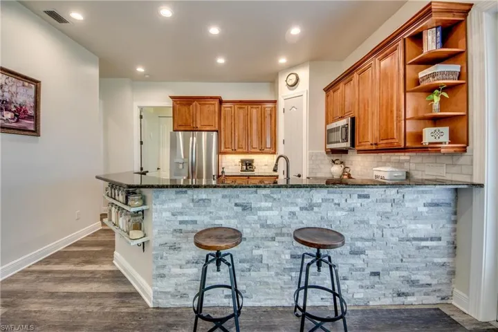 Kitchen featuring dark stone counters, stainless steel appliances, kitchen peninsula, and dark wood-type flooring
