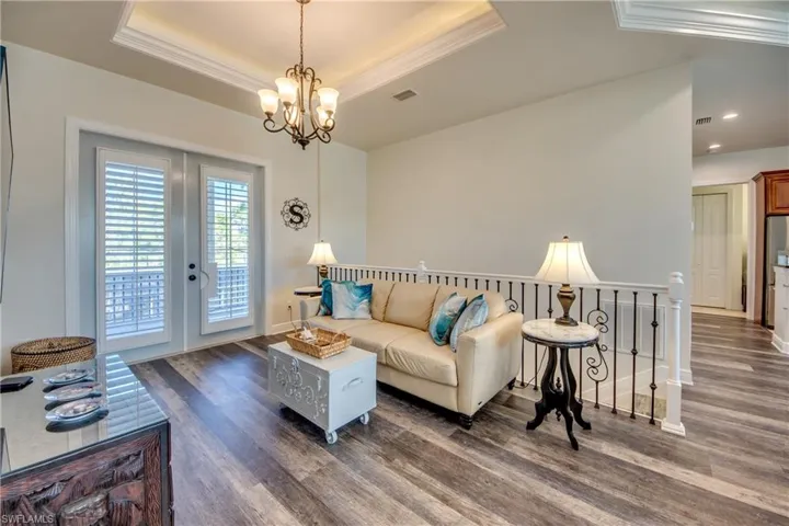 Living room featuring crown molding, dark hardwood / wood-style floors, a raised ceiling, and a notable chandelier