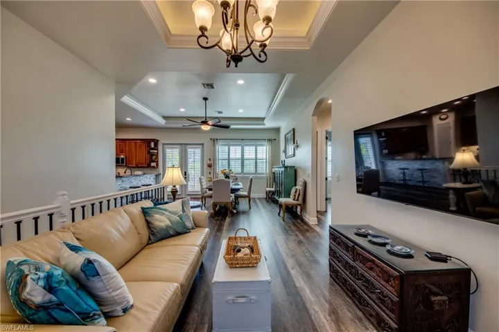 Living room featuring dark hardwood / wood-style flooring, ceiling fan with notable chandelier, and a tray ceiling