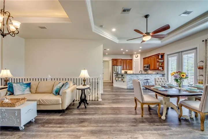 Dining space with crown molding, dark hardwood / wood-style floors, ceiling fan with notable chandelier, and a raised ceiling