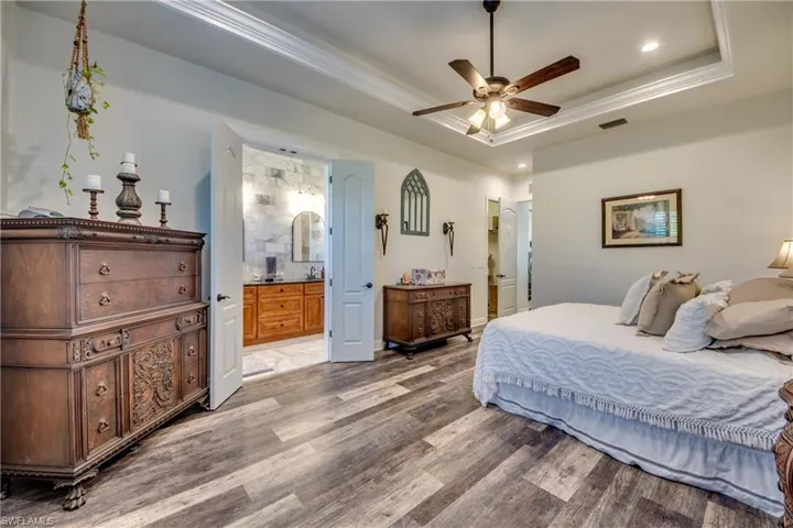 Bedroom with ceiling fan, ensuite bathroom, hardwood / wood-style flooring, and a tray ceiling