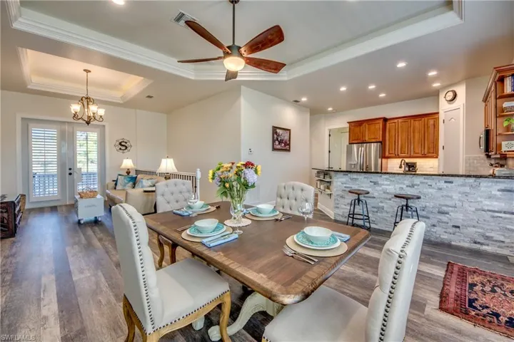 Dining space with ceiling fan with notable chandelier, hardwood / wood-style flooring, crown molding, and a tray ceiling